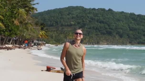 Jonge knappe blanke man rent en glimlacht op het strand op een zomerse dag — Stockvideo