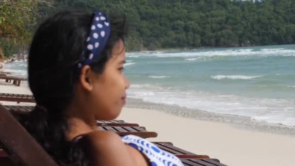 Közelkép oldalsó portré egy fiatal ázsiai nő ül a tengerparti padon. — Stock videók