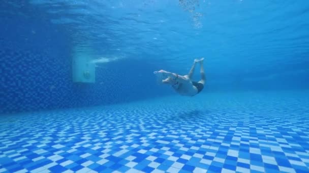 Молодий красивий лисий чоловік в окулярах і шортах плаває під водою в басейні . — стокове відео