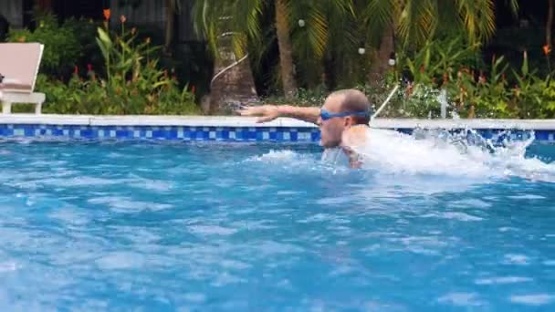 Een blanke man in gogless zwemmen in een buitenzwembad met tuin. — Stockvideo