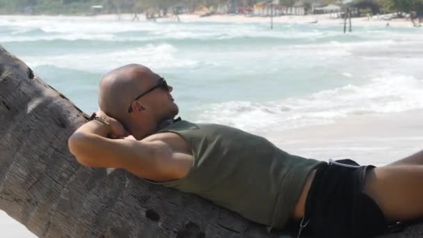 Fehér férfi feküdt a kókusz ág a strandon hullámok a háttérben — Stock videók