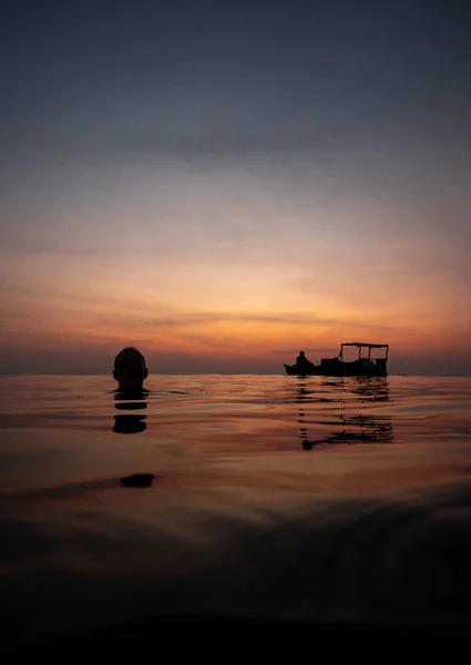 Fredfyldt udsigt ved havet i skumringen med en mand en fiskerbåd i det rolige vand. Stock-billede