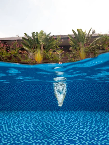 Split photography: Nierozpoznawalna osoba nurkująca w niebieskim basenie. Obraz Stockowy