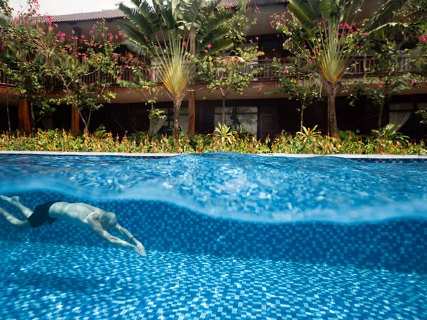 热带别墅，有鲜花和树木，还有一个男子游泳的原始游泳池. 图库图片