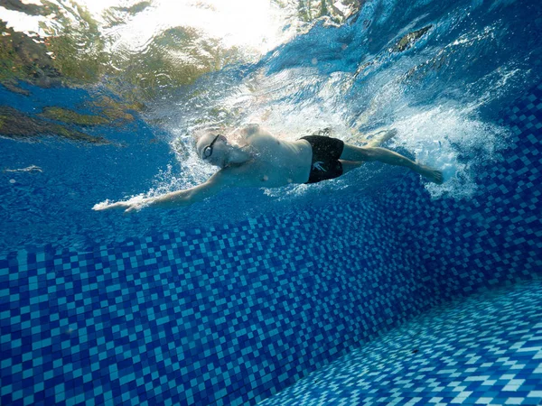 En hvid mand i korte og goggle svømning i den blå swimmingpool udendørs Stock-foto