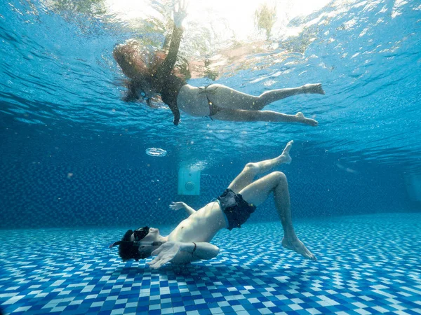 年轻男女们在清澈的蓝色游泳池里观看水下美景. 图库图片