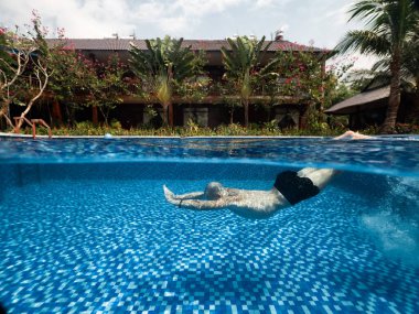 Tropikal bir villa ve el değmemiş yüzme havuzunda yüzen bir adam..