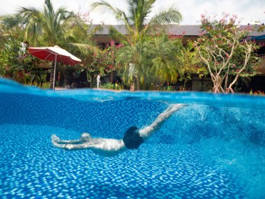 Tatil köşkündeki havuzda su altında çekilmiş bir adamın fotoğrafı.