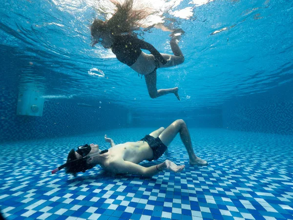 Vista submarina de hombre y mujer jóvenes en la piscina azul transparente. —  Fotos de Stock