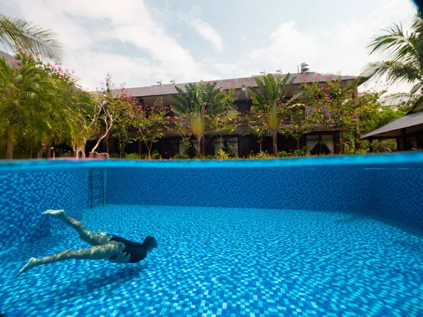 A woman in the bottom of the pool and view of tropical villa with green trees. Royalty Free Stock Images