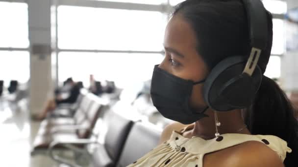 Nærbilde av en ung asiatisk kvinne med maske og hodetelefon på flyplassen. – stockvideo
