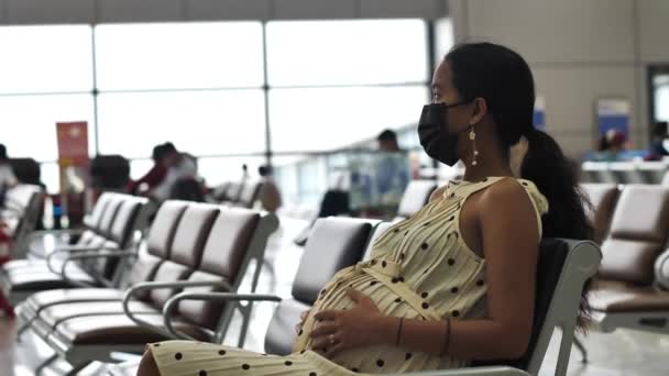 Pregnant young woman in mask sitting on the chair in the airport ddeparture area — Stock Video