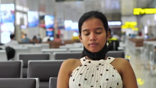 Азиатка сидит в зале ожидания аэропорта, снимает маску и дышит — стоковое видео