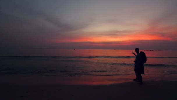 Vista cinematográfica de una joven pareja caminando por la playa y tomando fotos al atardecer — Vídeo de stock