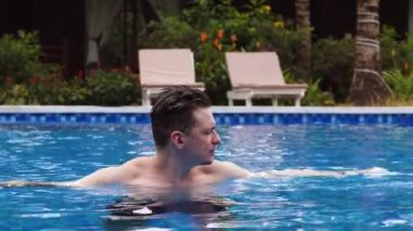 Genç yakışıklı beyaz adam güneşli bir günde havuzda banyo yapıyor ve dinleniyor..