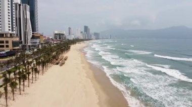 Şehir plajında uzun ve geniş bir manzaranın havadan sinemasal görüntüsü, kumlara vuran büyük dalgalar..