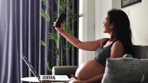 Gravid kvinna sitter på soffan ta selfie och bilder av hennes stora mage. — Stockvideo