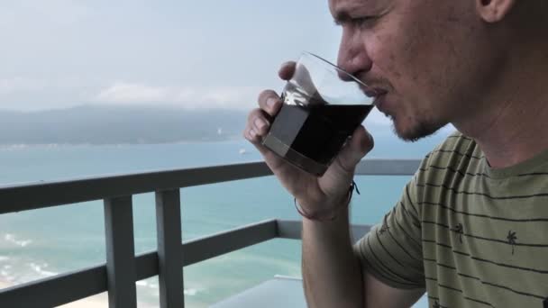 Kaukasier trinkt Kaffee auf Balkon mit herrlichem Blick auf Meer und Berge. — Stockvideo