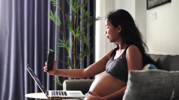 Ung gravid kvinde sidder på sofaen i stuen tager selfie billeder. – Stock-video