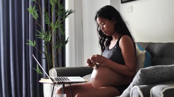 Gravid kvinde, der arbejder hjemme, drikker sine vitaminer og rører ved hendes store mave. – Stock-video