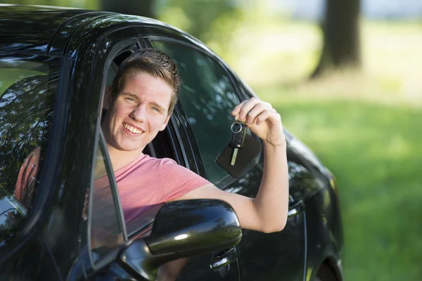 Joven mostrando llaves mientras está sentado en un coche nuevo — Foto de Stock