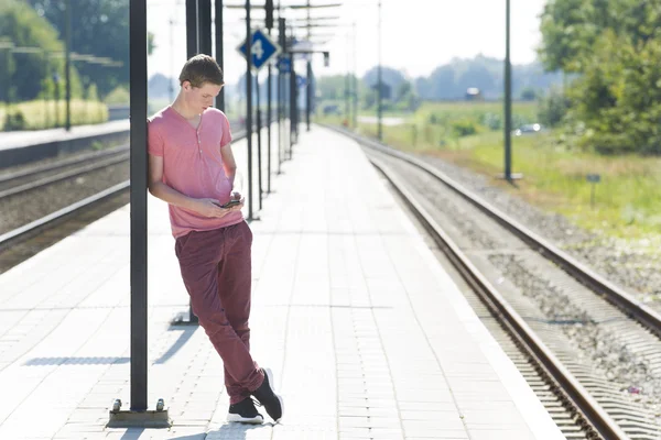 Людина використовує мобільний телефон під час очікування залізничної платформи — стокове фото