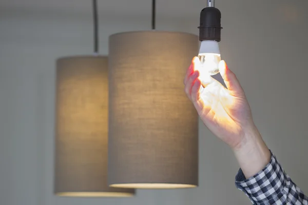 Mão ajustando lâmpada elétrica por luzes pingente em casa Fotografia De Stock