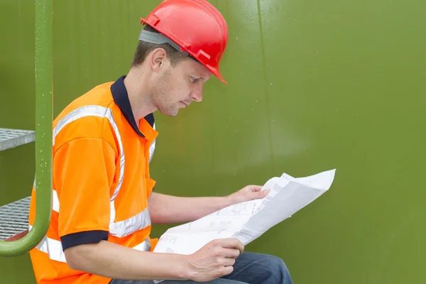 Arquitecto masculino examinando el plano mientras está sentado en los pasos Imagen De Stock