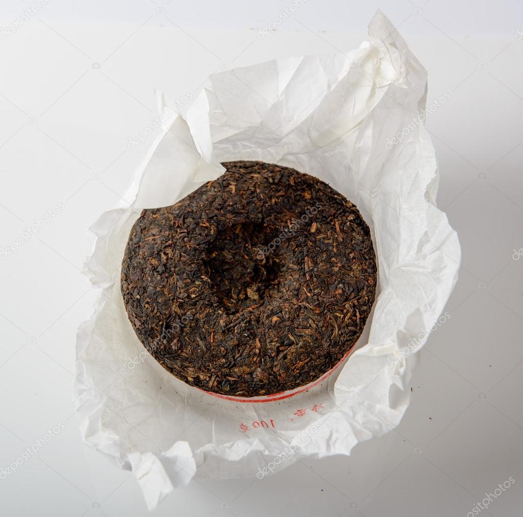 chinese puer tea cake in unwrapped packing on white background