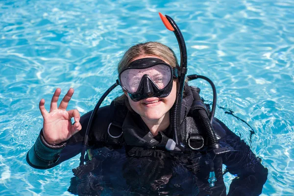 スキューバダイバーでプールで彼女のダイビングマスクで見ます上のカメラの笑顔とショーをOkサイン — ストック写真