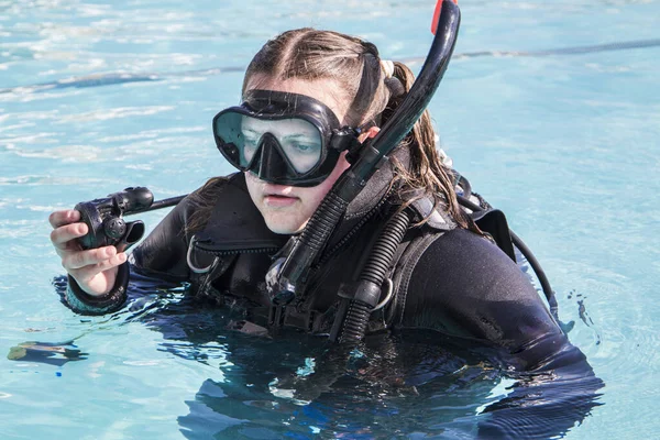 Scuba dive training in a pool, a student with a wetsuit and dive mask on and regulator in her hand close up.