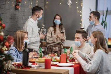 Coronavirüslü bira partisi. Bir grup genç insan birayla kadeh kaldırıyor. Arkadaşlar Covid-19 koruyucu maskelerle bira şişelerini tokuşturuyor.