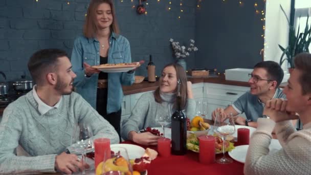 En vacaciones, una chica trae pizza. Amigos se reunieron en una mesa grande. Come, bebe y diviértete. — Vídeos de Stock