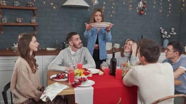 Em um feriado, uma garota traz pizza. Amigos se reuniram em uma grande mesa. Comer, beber e se divertir — Vídeo de Stock