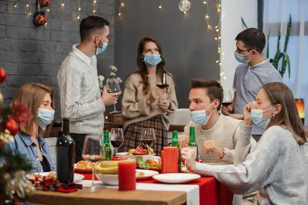 Beer party with the coronavirus. A group of young people raise toasts with beer. Friends clinking beer bottles in Covid-19 protective masks