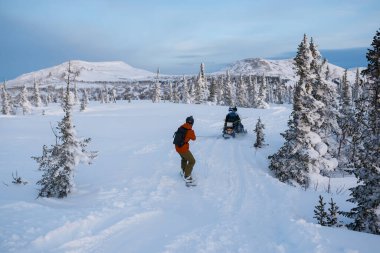 Snowboardcu elinde halatla kar aracına biniyor. Güzel karlı ormanın arasındaki donmuş gölde. Aşırılık.