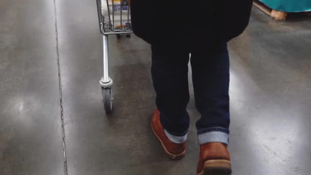 A man pushes a cart in a supermarket. Close-up shot of the legs — Stock Video