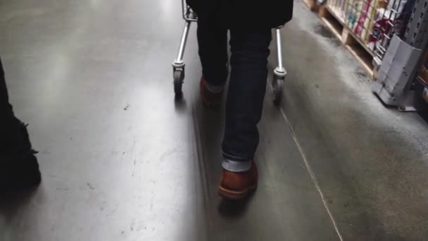 Um homem empurra um carrinho num supermercado. Close-up tiro das pernas — Vídeo de Stock