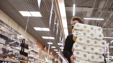 2019-2021 karantinasında Coronavirus COVID-19 salgını sırasında elinde tuvalet kağıdı torbalarıyla tıbbi maskeyle yürüyen bir adam.