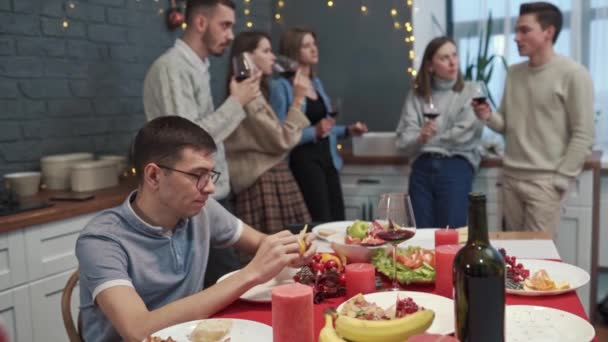 Sorglig kille med stressat ansikte sitter ensam medan glada vänner har kul på fest äta dricka och skratta. Ensamhet och problem koncept — Stockvideo