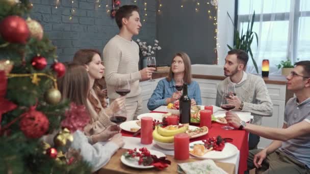 Grupa przyjaciół świętuje Nowy Rok. Młody człowiek wstaje i wznosi toast — Wideo stockowe