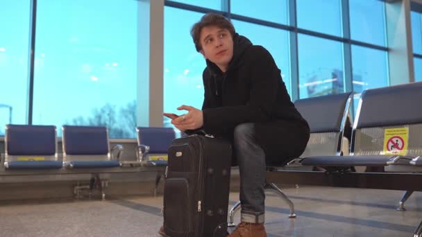 Νεαρός επιχειρηματίας περιμένει για καθυστερημένη πτήση αεροπλάνο στο αεροδρόμιο σύγχρονη αίθουσα αναμονής γεμάτη με επιβάτες. — Αρχείο Βίντεο