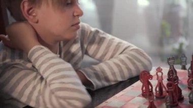 Evde satranç oynayan zeki çocuk, satranç tahtasının bir parçasını hareket ettiriyor.