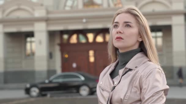 Een meisje met blond haar staat vlakbij een prachtig gebouw — Stockvideo