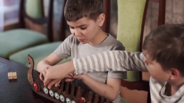 Δύο αγόρια παίζουν ένα παλιό επιτραπέζιο παιχνίδι των Βίκινγκ. Ένα ξύλινο πλοίο με πολέμους — Αρχείο Βίντεο