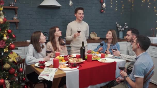 Grupa przyjaciół świętuje Nowy Rok. Młody człowiek wstaje i wznosi toast — Wideo stockowe