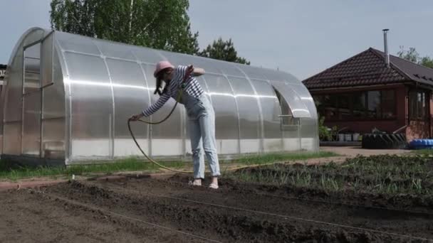 Mladý usmívající se dívka zalévání zahrada od zahradní hadice v horkém letním dni. — Stock video