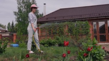 Sıcak bir yaz günü bahçe hortumundan bahçeyi sulayan genç bir kız..