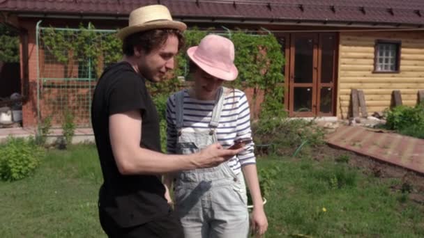 Un jeune couple dans la cour de leur maison regarde le téléphone et rit. — Video