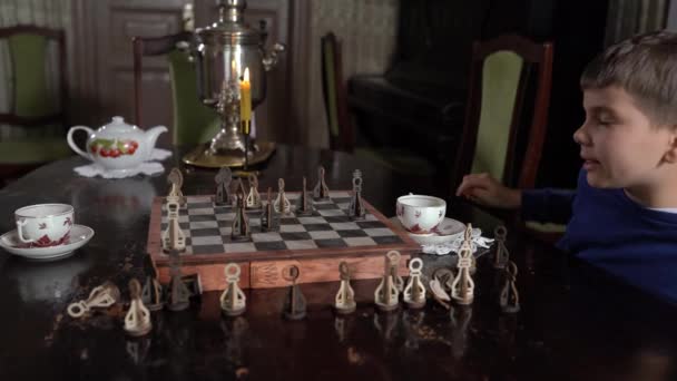 Vista lateral bonito pequeno 6s filho e jovem pai jogar xadrez sentado interior. — Vídeo de Stock